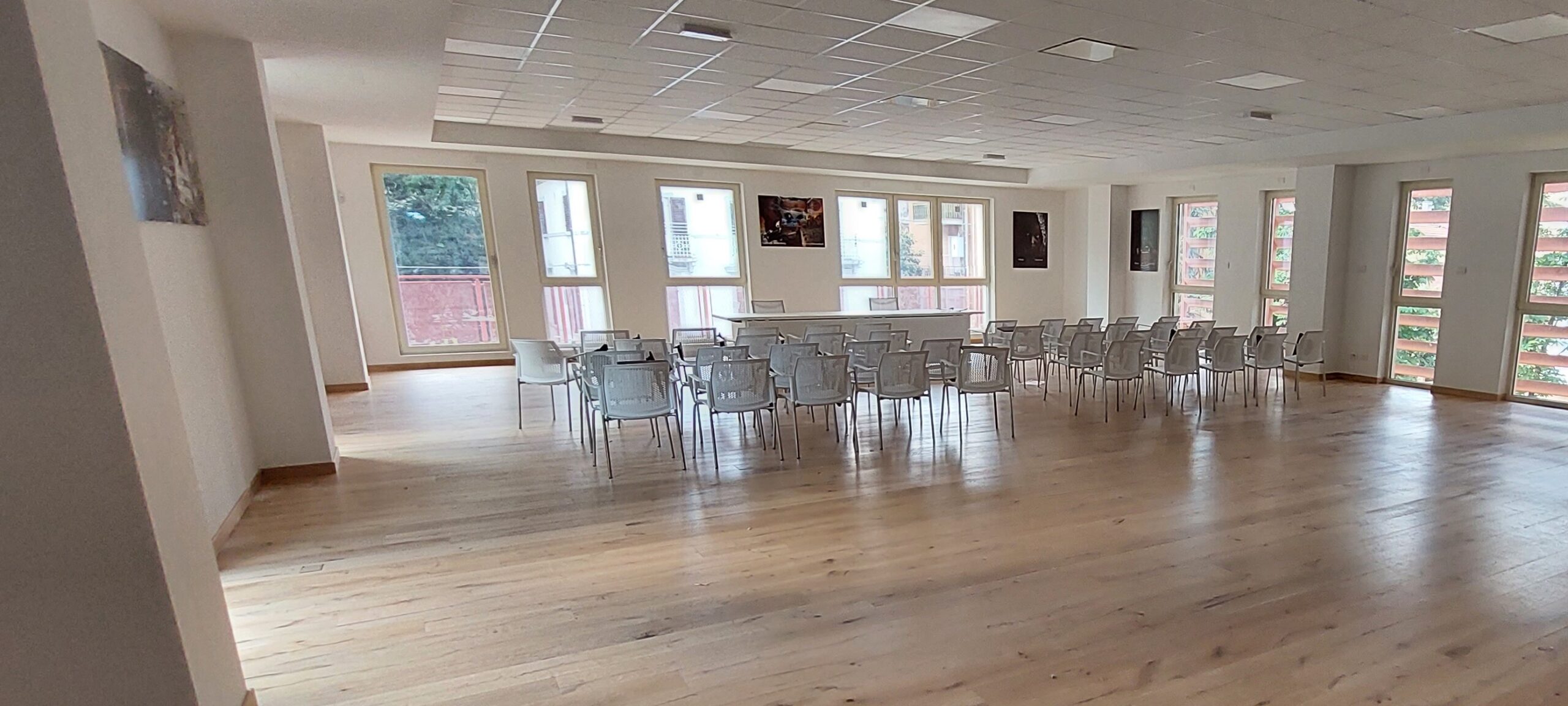 Un grande salone illuminato da grandi finestre, con pavimento in parquet e sedie da conferenza 