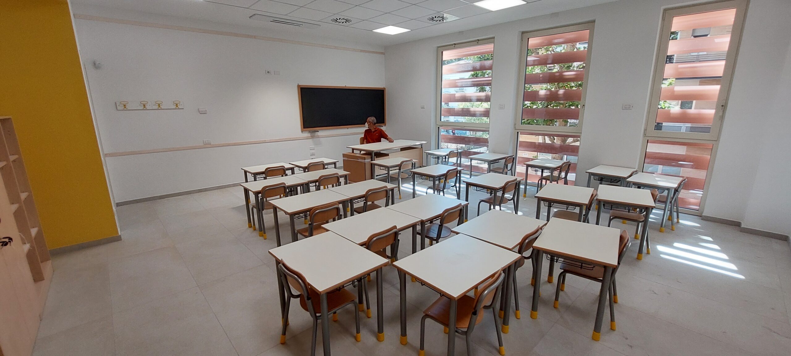 Un'aula con i banchi e le grandi finestre ombreggiate