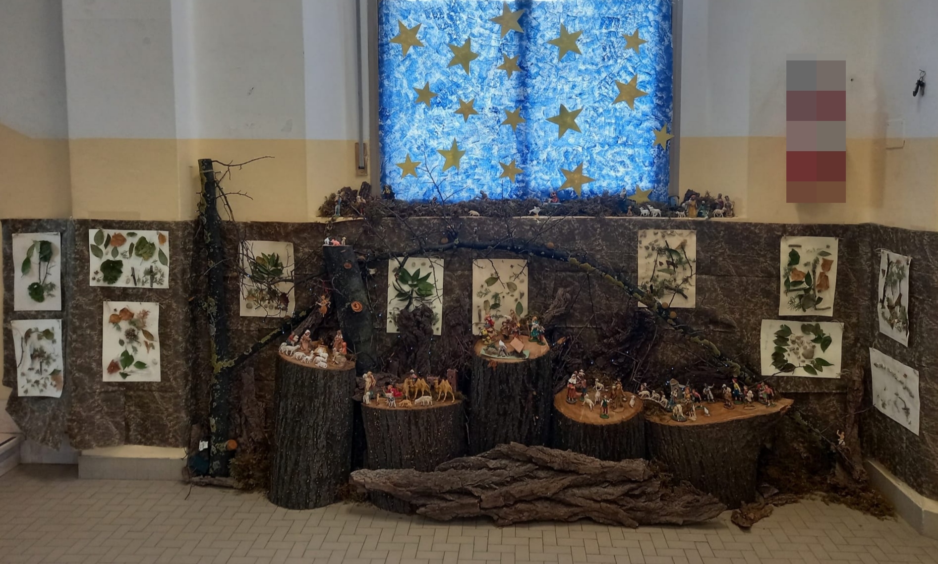 Il presepio della scuola de Amicis: le statuine sono disposte sui pezzi di tronco di un albero. Sullo sfondo la carta color verde/marrone con applicate foglie di varie piante