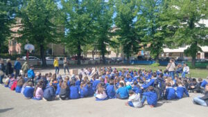 Gli alunni della scuola Toti riuniti nel cortile e seduti a terra in semicerchio durante la giornata conclusiva del progetto Laboratorio delle idee