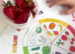 Un cestino di fragole sulla tovaglietta raffigurante frutta e verdura sul banco di un alunno 